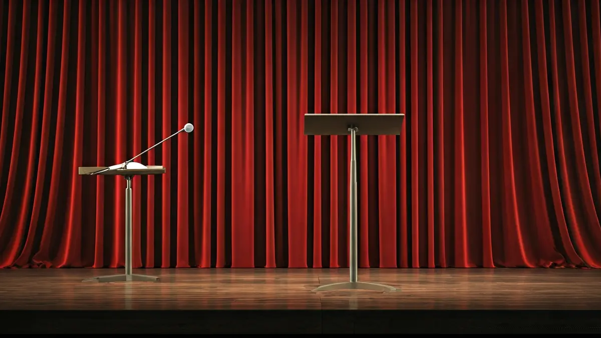 Imagen genérica de un escenario de concierto con un atril y un podio de director, cortinas de terciopelo rojo al fondo.