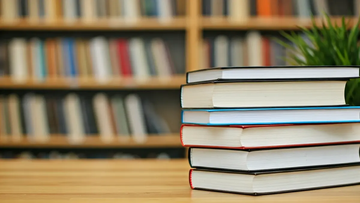 Imagen genérica de libros apilados en una mesa de madera en un ambiente de biblioteca.