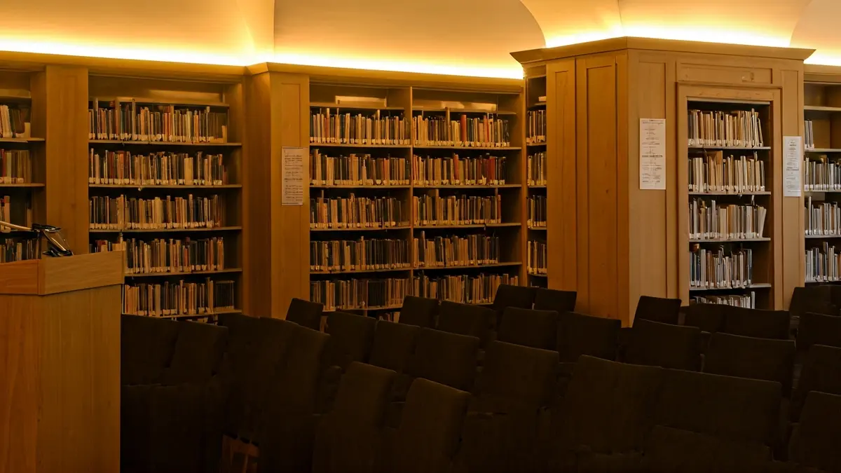 Imagen genérica de un interior de biblioteca con estanterías de madera y un podio con micrófono.