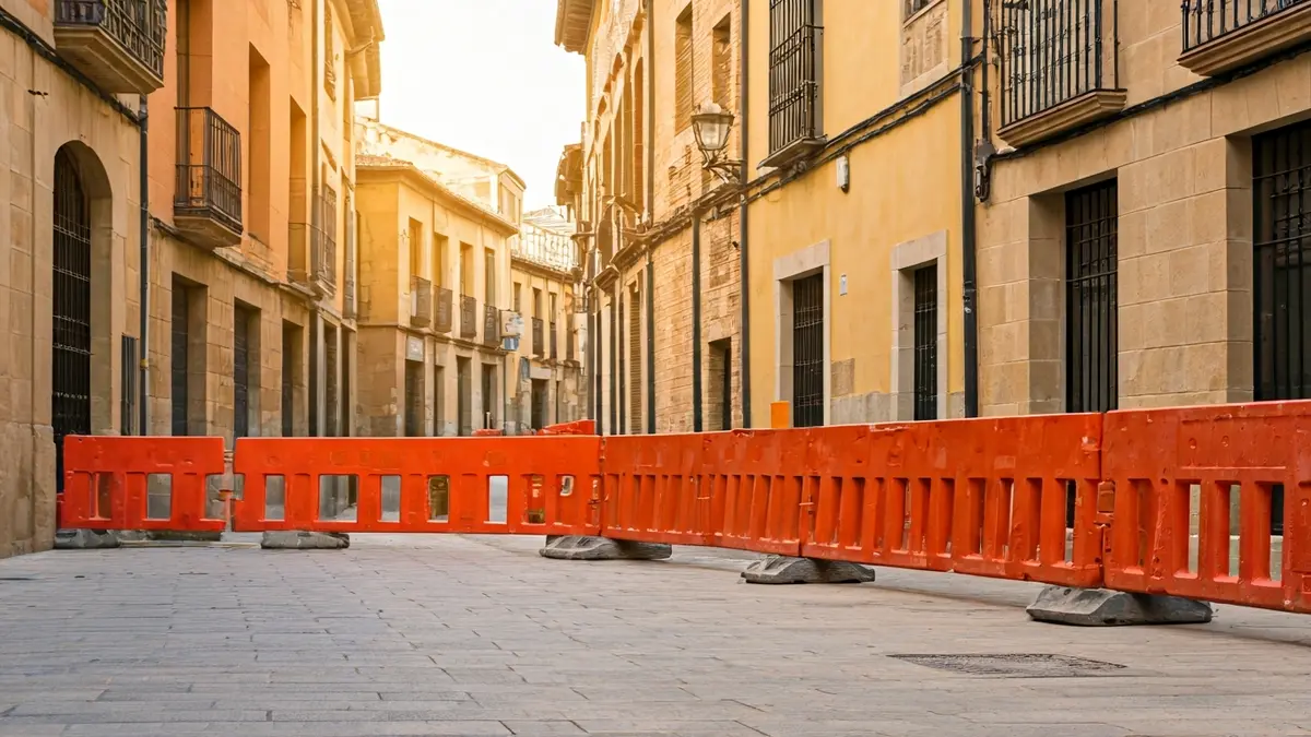 Image of a street under construction in a Spanish town, with orange barriers and scaffolding.