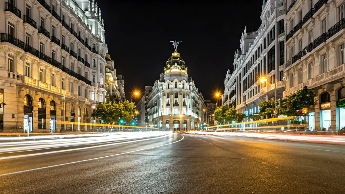 Vista nocturna de la Gran Vía de Madrid con sus edificios históricos iluminados y el movimiento de la ciudad.