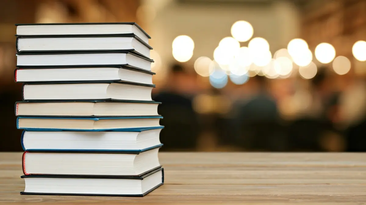 Imagen genérica de una pila de libros en una mesa de madera en una biblioteca.