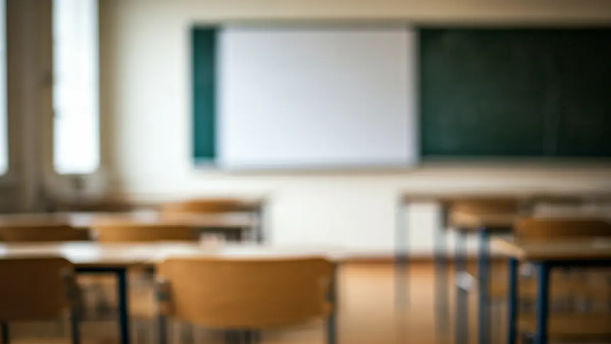 Imagen genérica de un aula vacía, con pupitres y una pizarra, iluminada por luz natural.