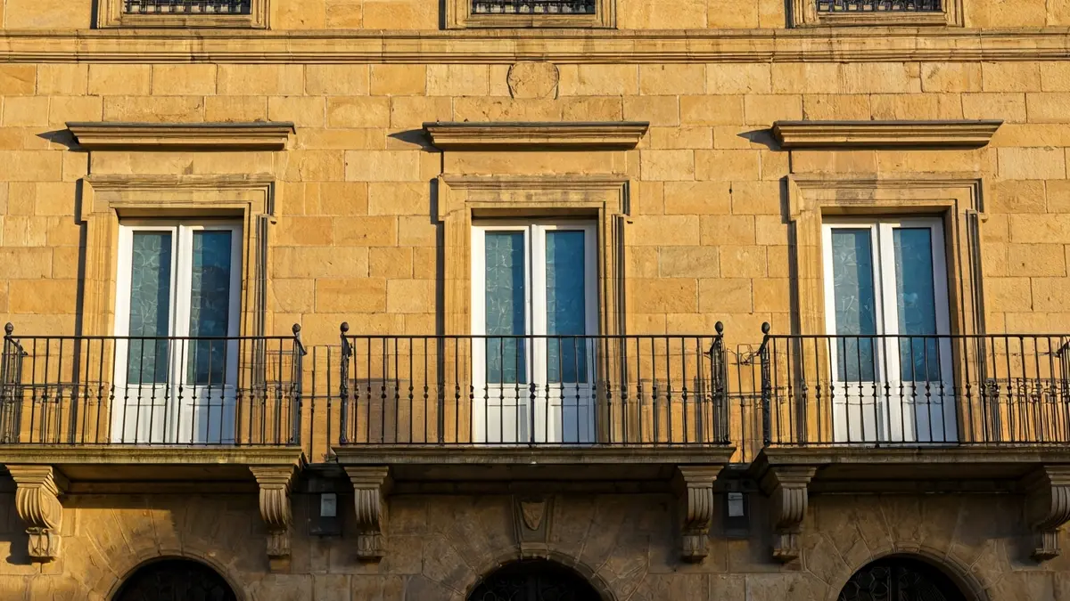 Stone town hall facade with balcony and iron railings, under afternoon sunlight.