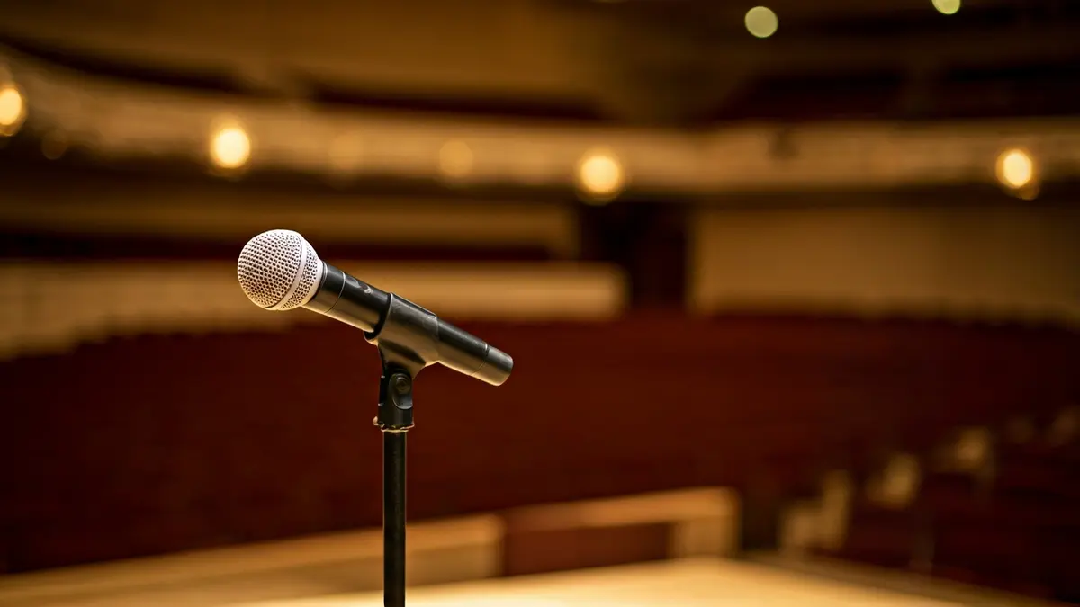 Imagen genérica de un micrófono en un escenario de concierto, con asientos vacíos al fondo.