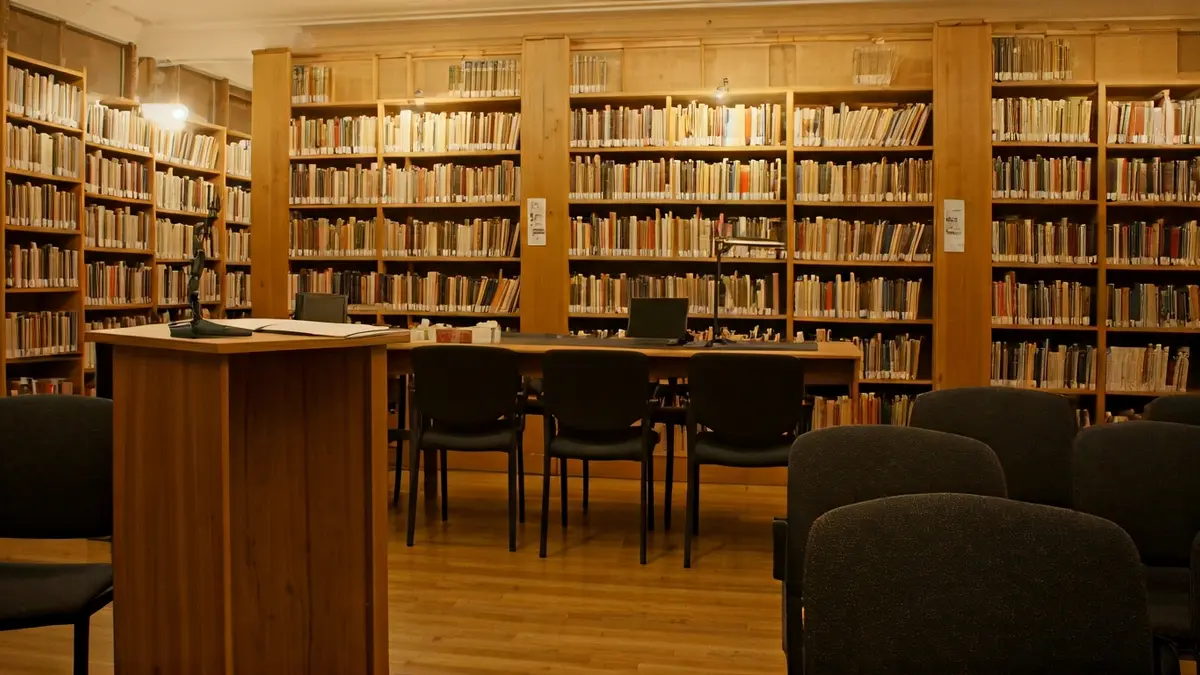 Generic image of a library interior with wooden bookshelves and a microphone podium, evoking a cultural atmosphere.