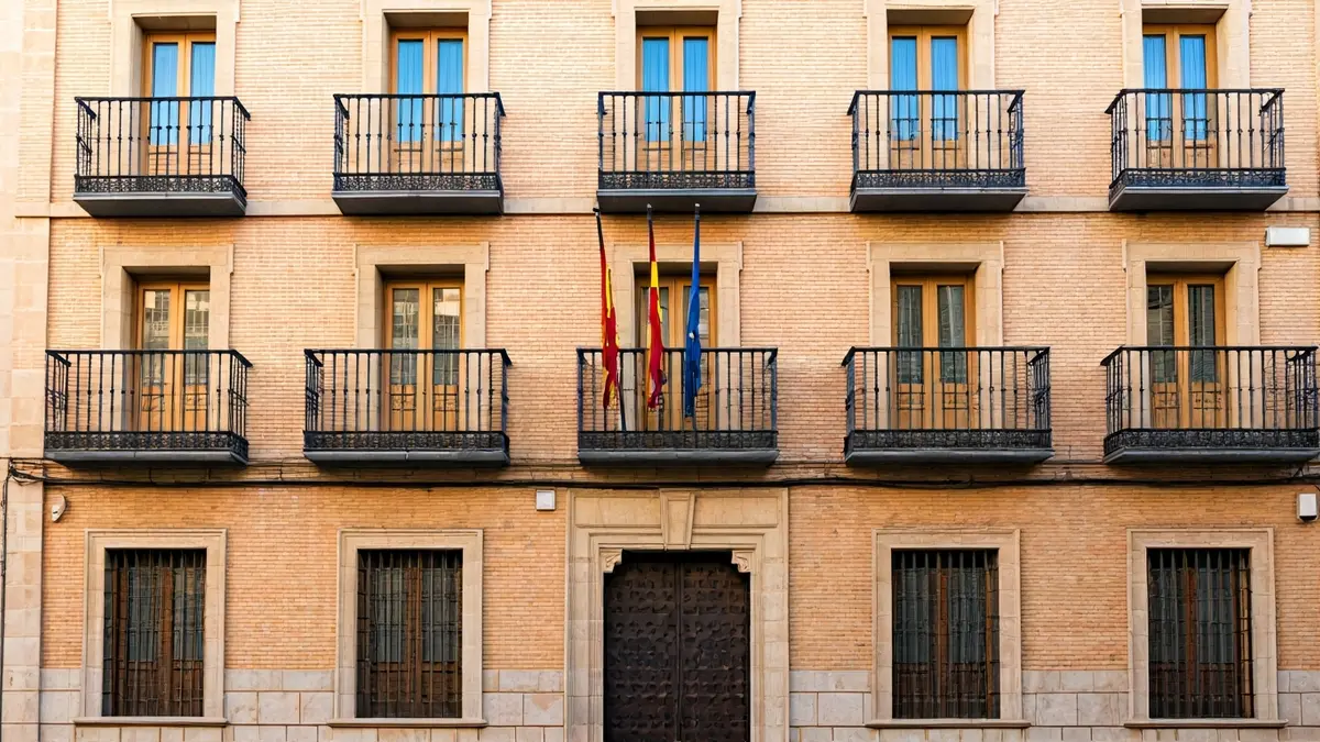 Fachada de un ayuntamiento con balcones y barandillas de hierro, bajo la luz del sol de la tarde.
