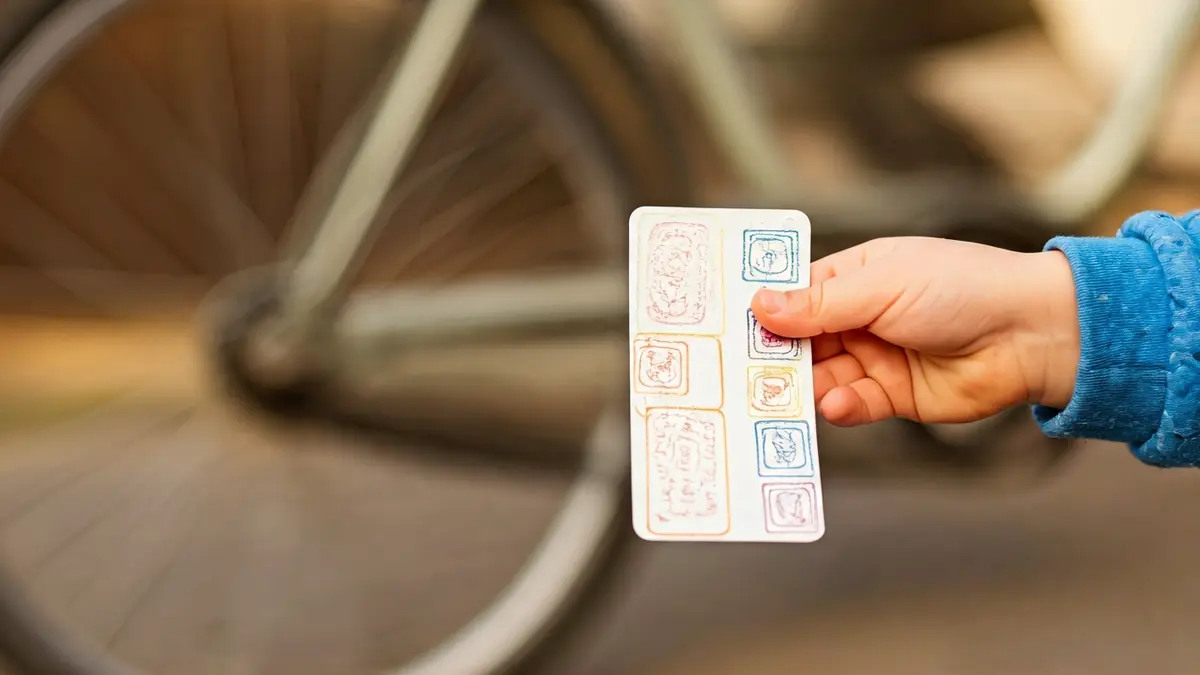 Generic image of a child's hand holding a reward card with stamps, with a blurred bicycle in the background.