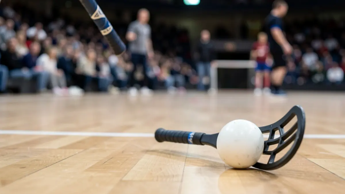 Primer plano de un stick y una pelota de floorball sobre una cancha de madera.