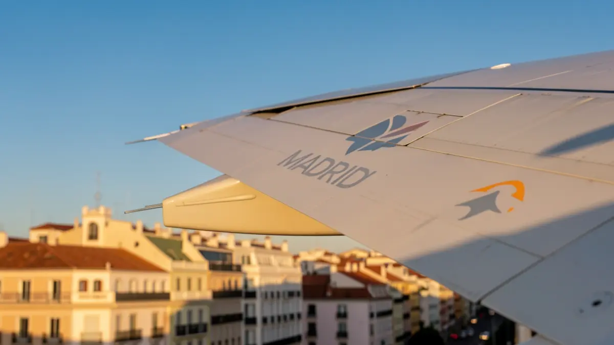 Airplane wing with the Community of Madrid logo over urban architecture.