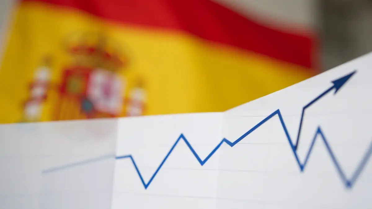 Gráfico abstracto de tendencia descendente con una bandera española difuminada al fondo.