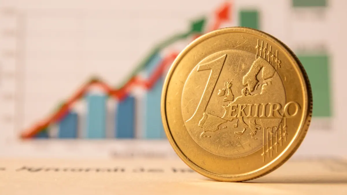 Primer plano de una moneda de euro española con un gráfico de inflación ascendente al fondo.