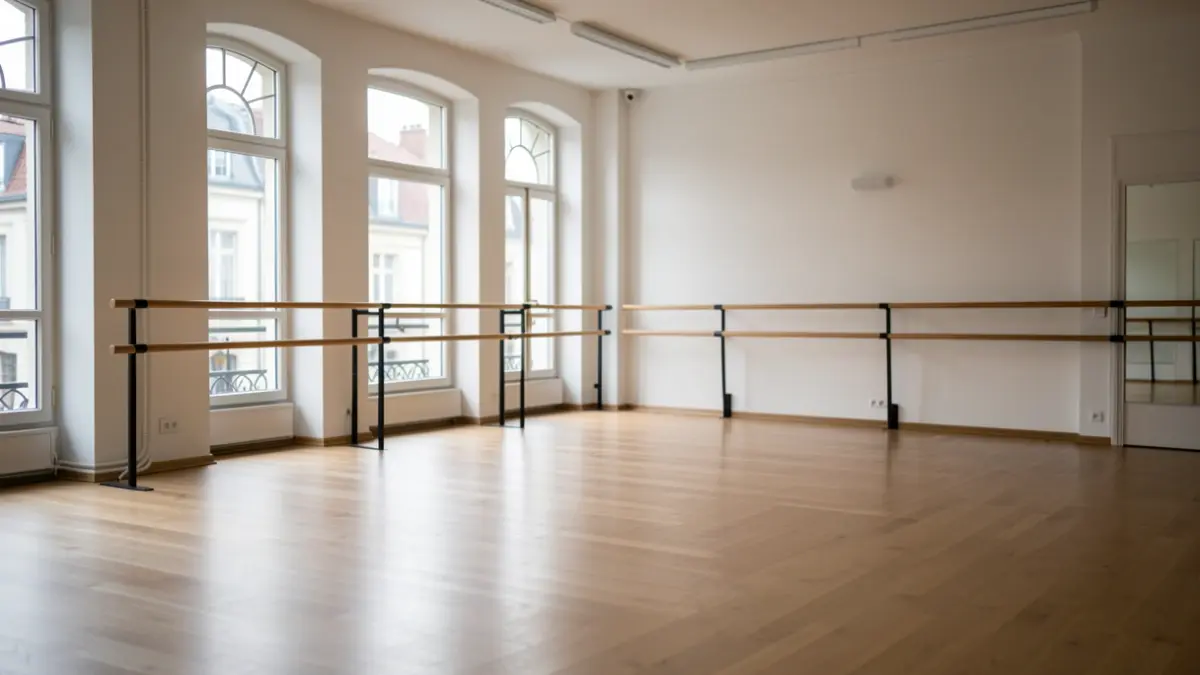 Empty contemporary dance studio with wooden floor and ballet barres, illuminated by natural light.
