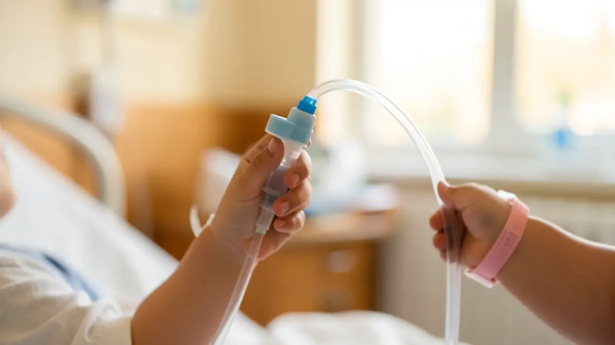 Imagen genérica de una mano infantil sujetando un dispositivo médico con un fondo hospitalario desenfocado.